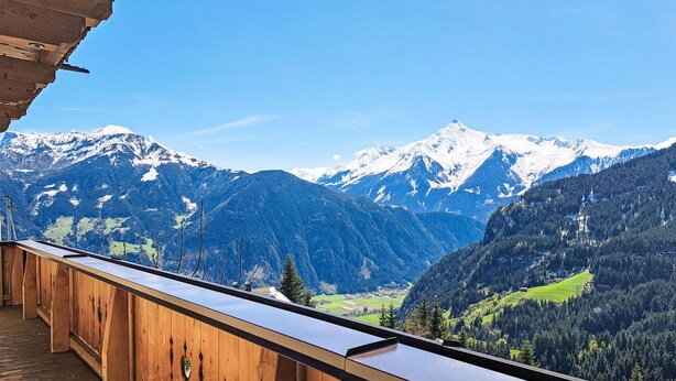 Un balcone in legno con vista su montagne innevate e una valle sottostante.