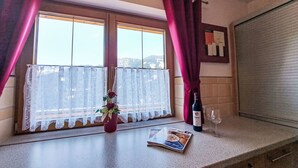 Una cucina con una finestra, una rivista sul bancone, una bottiglia di vino e un vaso con fiori.