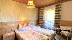 A room with a wooden ceiling, a bed with floral bedding, a nightstand, a chair, and a table with a tablecloth. - Schusterhäusl by Interhome (Mayrhofen)