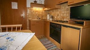 A compact kitchen with wooden cabinets, a built-in oven, a sink, and a television.