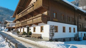 A traditional wooden chalet with a balcony, white walls, and a snow-covered roof.