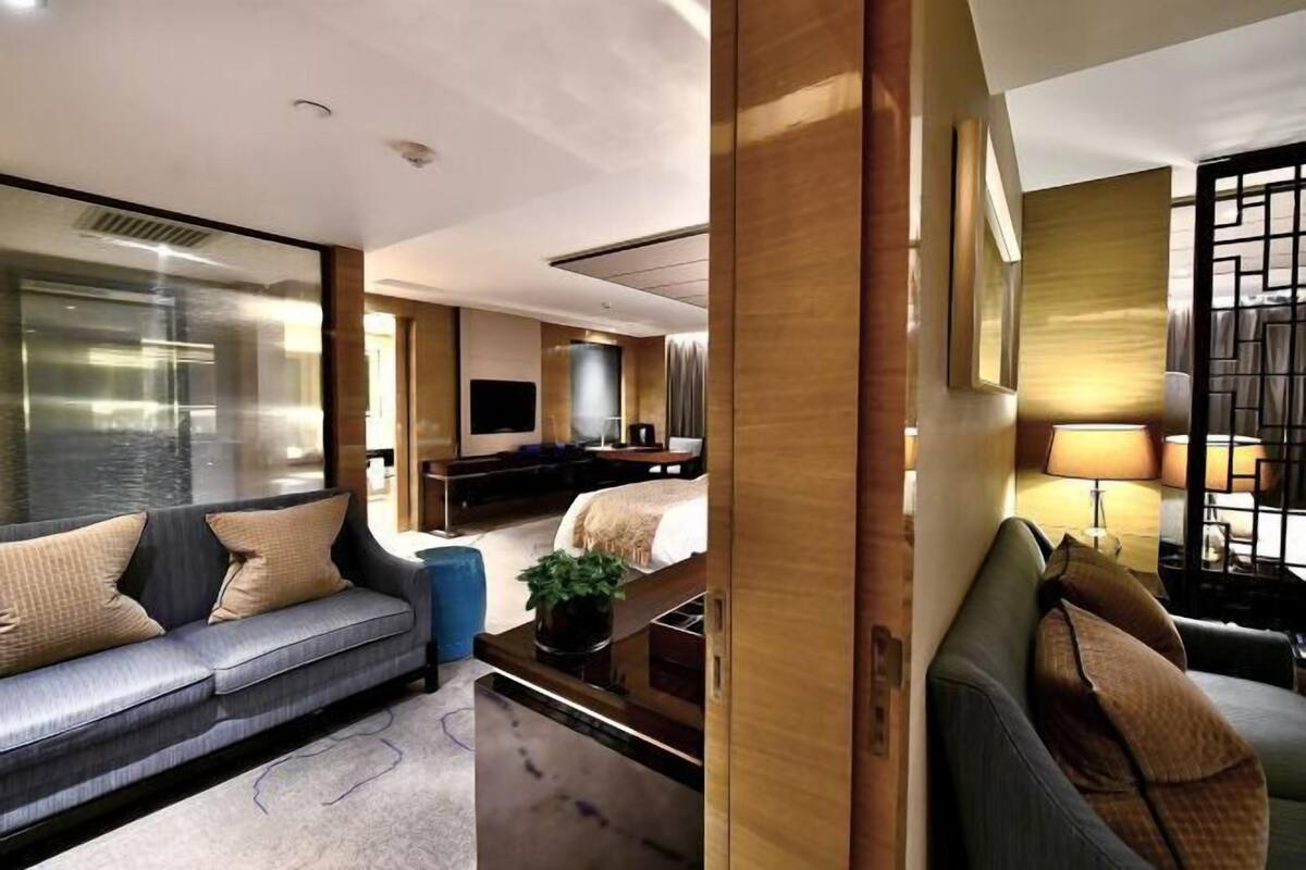 Ein modernes Hotelzimmer mit Sofa, Bett, Fernseher und Schreibtisch mit Lampe.