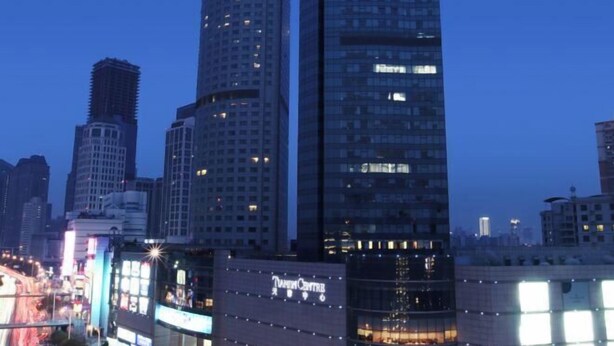 Un edificio alto con fachada de vidrio moderna, rodeado de otros edificios altos en un paisaje urbano.