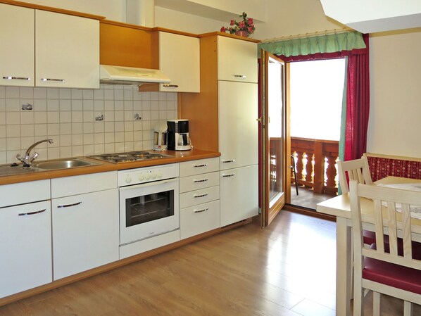 A kitchen with white cabinets, a stove, and a sink. There is a dining area with a table and chairs. - Heisenhaus by Interhome (Mayrhofen)
