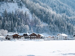 A row of wooden cabins with snow-covered roofs, set against a backdrop of a snow-covered forest and mountains. - Heisenhaus by Interhome (Mayrhofen)