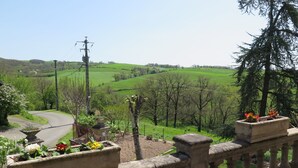 A balcony with a stone balustrade overlooking a green landscape with a winding road and trees.