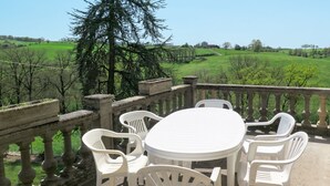 A round table with six white plastic chairs on a balcony with a stone balustrade.