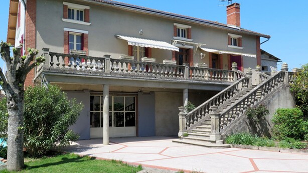 A two-story building with a balcony, a staircase, and a covered entrance.