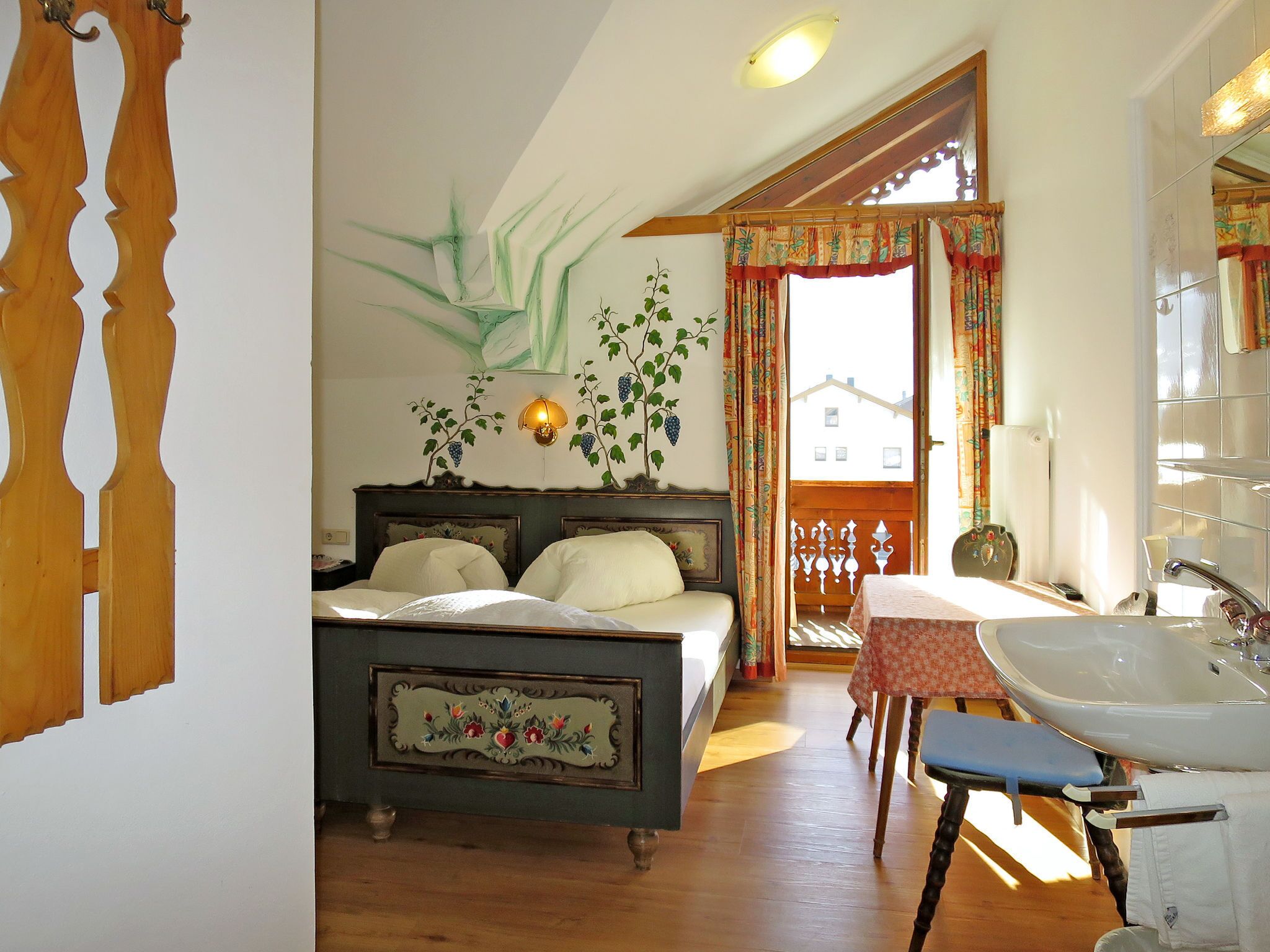 Een slaapkamer met een bed, een nachtkastje, een raam met gordijnen, een wandlamp en uitzicht op buiten.