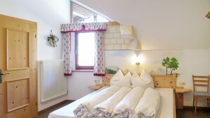 A wooden bed with white bedding, a window with floral curtains, a radiator, and a small plant on the nightstand.