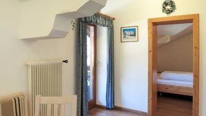 A room with a wooden floor, a radiator, a bed, and a door leading to another room.