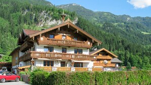 A traditional wooden chalet with a balcony, set against a mountainous backdrop.