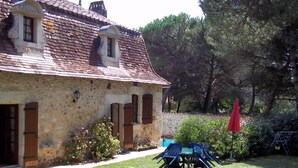 Una casa de piedra con tejado de baldosas, un jardín con una mesa y sillas, y un paraguas rojo.