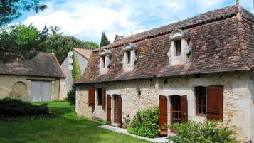 A rustic stone building with a tiled roof, wooden shutters, and a small garden area.