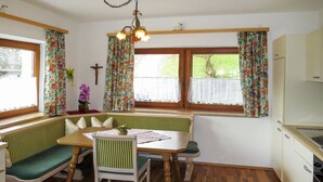 A cozy kitchen with a wooden table, green cushioned bench, and a window with floral curtains. - Brugger by Interhome (Mayrhofen)