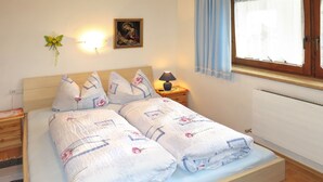 A neatly made bed with floral bedding, a wall-mounted picture, a bedside lamp, and a window with curtains. - Brugger by Interhome (Mayrhofen)