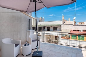 A balcony with a white chair, a small table, and a large umbrella.