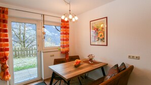 A dining area with a wooden table, chairs, a bench, a chandelier, a window with curtains, and a framed picture on the wall. - Apartment Bair by Interhome (Mayrhofen)