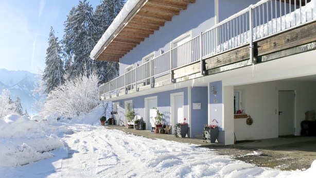 A hotel with a covered balcony, potted plants, and a snowy landscape. - Apartment Bair by Interhome (Mayrhofen)