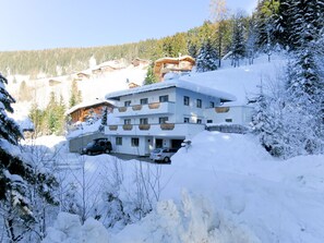 A multi-story hotel with a snow-covered roof, surrounded by trees and other buildings in a mountainous area.