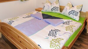 Una cama individual con colchón verde, ropa de cama blanca y verde estampada, y almohadas a juego. Hay dos mesitas de noche con lámparas, una ventana con cortinas y un cabecero de madera.