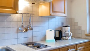 Et køkken med træskabe, en stålvask, et indbygget emfang og en kaffemaskine på bordpladen.