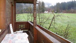 En træterrasse med et bord og stole, med udsigt over en græsplæne og et skovområde.