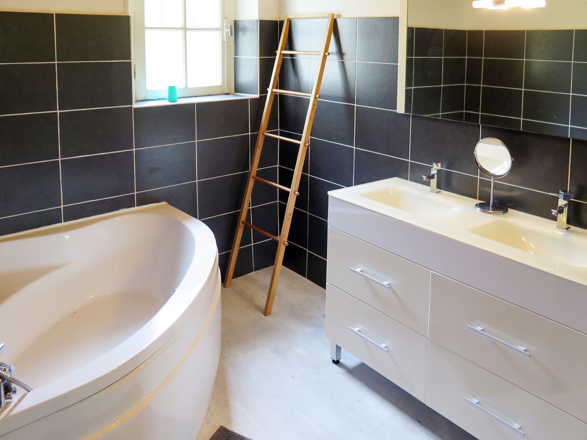 A bathroom with a bathtub, a vanity with a mirror, and a ladder leaning against the wall.
