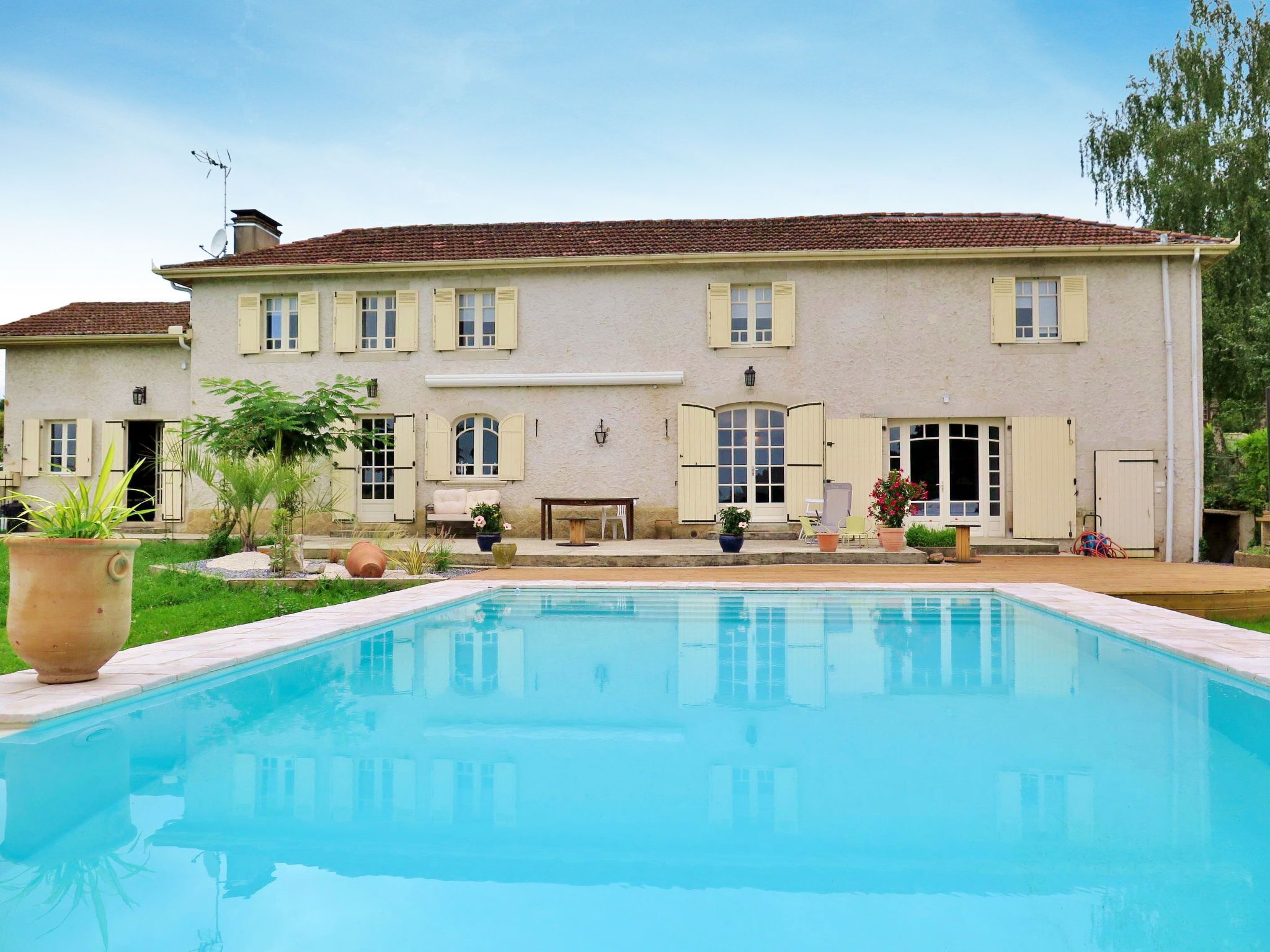 A large building with a swimming pool in front, featuring multiple windows and doors, and outdoor seating areas.