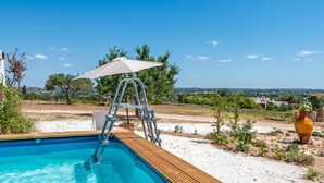 Una piscina con cubierta de madera, una escalera y una sombrilla blanca.