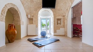 Una habitación amplia con pared de piedra, televisor montado en la pared y una alfombra de ejercicios, además de un jarrón grande.