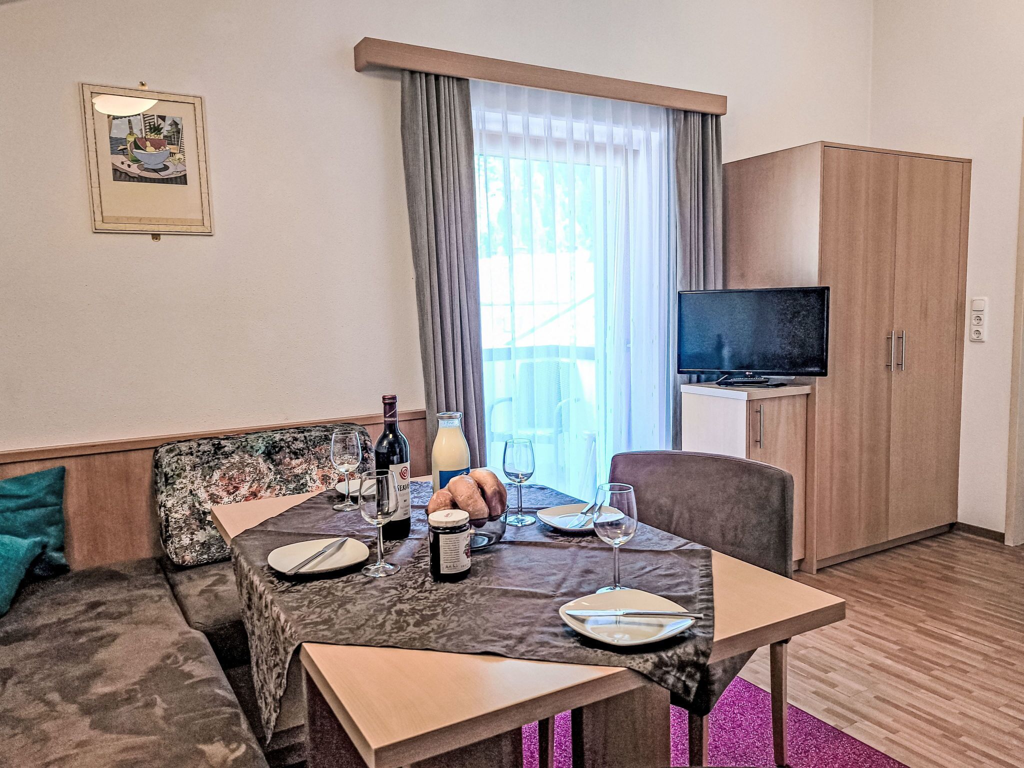 Ein Hotelzimmer mit Esstisch für zwei Personen, einer Couch, einem Fernseher und einem Schrank.