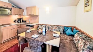 A compact kitchen with wooden cabinets, a microwave, and a coffee maker. There is a dining table with chairs and a sofa with a floral cushion. - Apartment Rosa by Interhome (Mayrhofen)