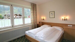 A hotel room with a large bed, two bedside tables, a radiator, and a window with curtains. - Apartment Rauter by Interhome (Mayrhofen)