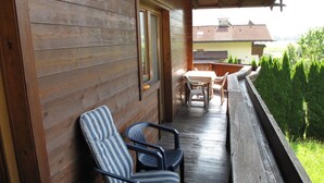 Un balcon en bois avec deux chaises à rayures, une table et une vue sur une maison et des arbres.