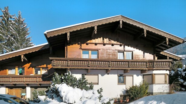 Un chalet en bois doté d’un balcon, entouré d’arbres couverts de neige et surplombant un ciel bleu clair.