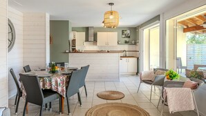 Una cocina moderna con armarios blancos, una isla central y un comedor con sillas de mimbre y una mesa preparada para cuatro.