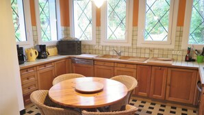 A kitchen with wooden cabinets, a round dining table with wicker chairs, a black microwave, and a window with a view of greenery.