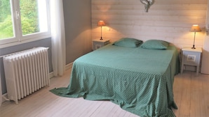 A bedroom with a bed, two bedside tables with lamps, a radiator, and a window with curtains.