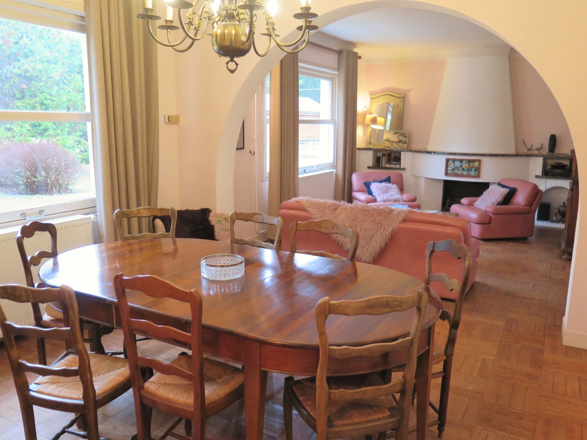 A dining area with a wooden table and chairs, a chandelier, and a cozy living room with a fireplace and seating.