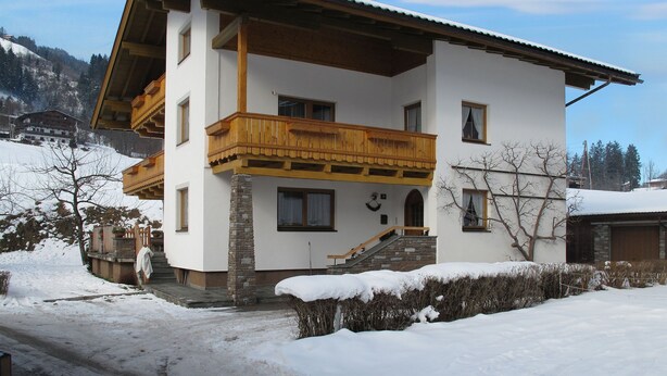 Un chalet à deux étages doté d’un balcon en bois, d’un pilier en pierre et surplombant un paysage enneigé.