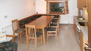 Une cuisine compacte avec un coin repas, comprenant une table et des chaises en bois, un four encastré et une fenêtre avec des rideaux.