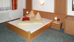 Un lit simple avec un cadre en bois, une table de chevet avec une lampe, un radiateur et une fenêtre avec des rideaux.