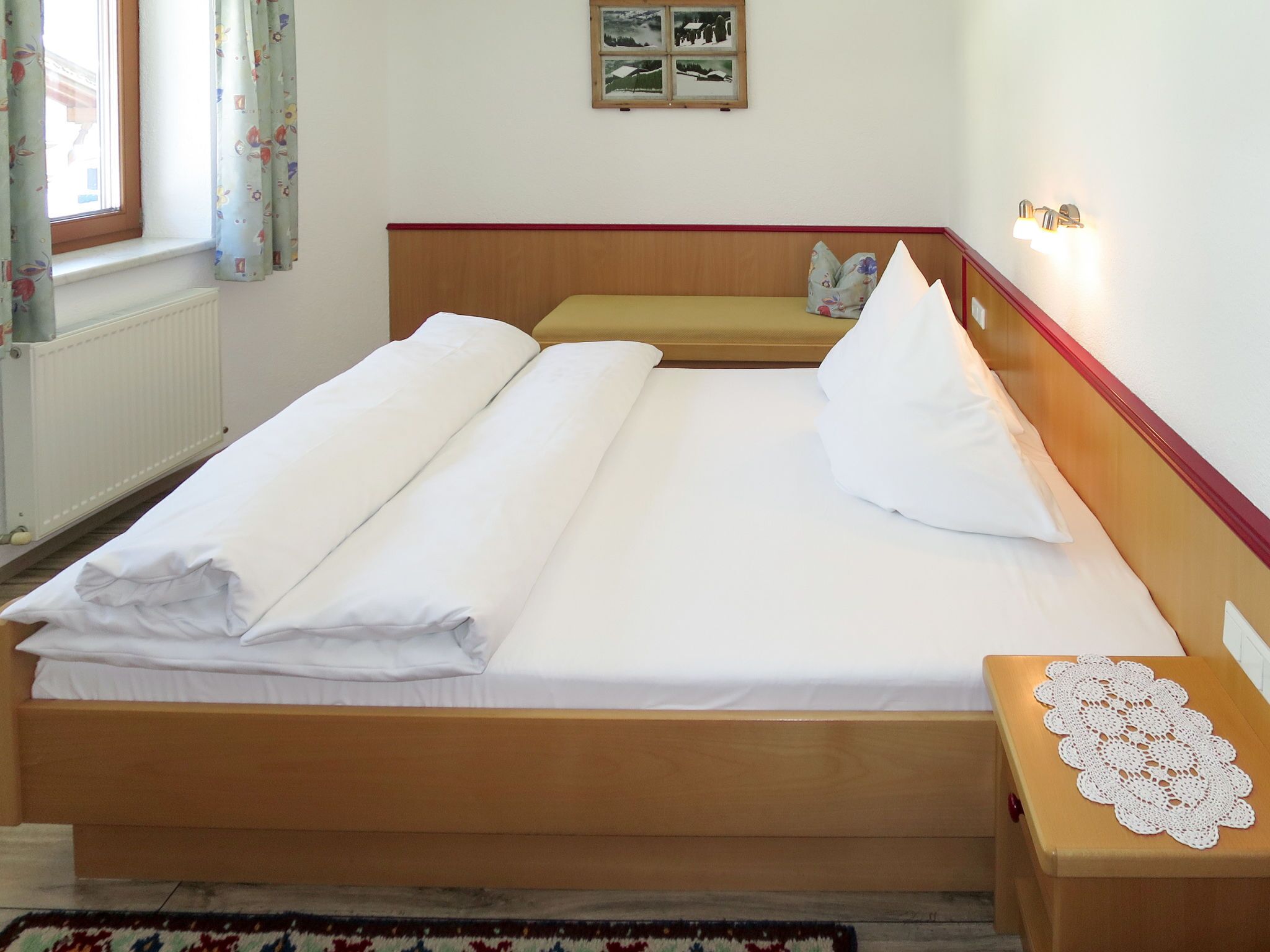 Ein ordentlich bezogenes Bett mit weißen Leinen, ein hölzernes Kopfende und ein Nachttisch mit einer Spitzendecke.