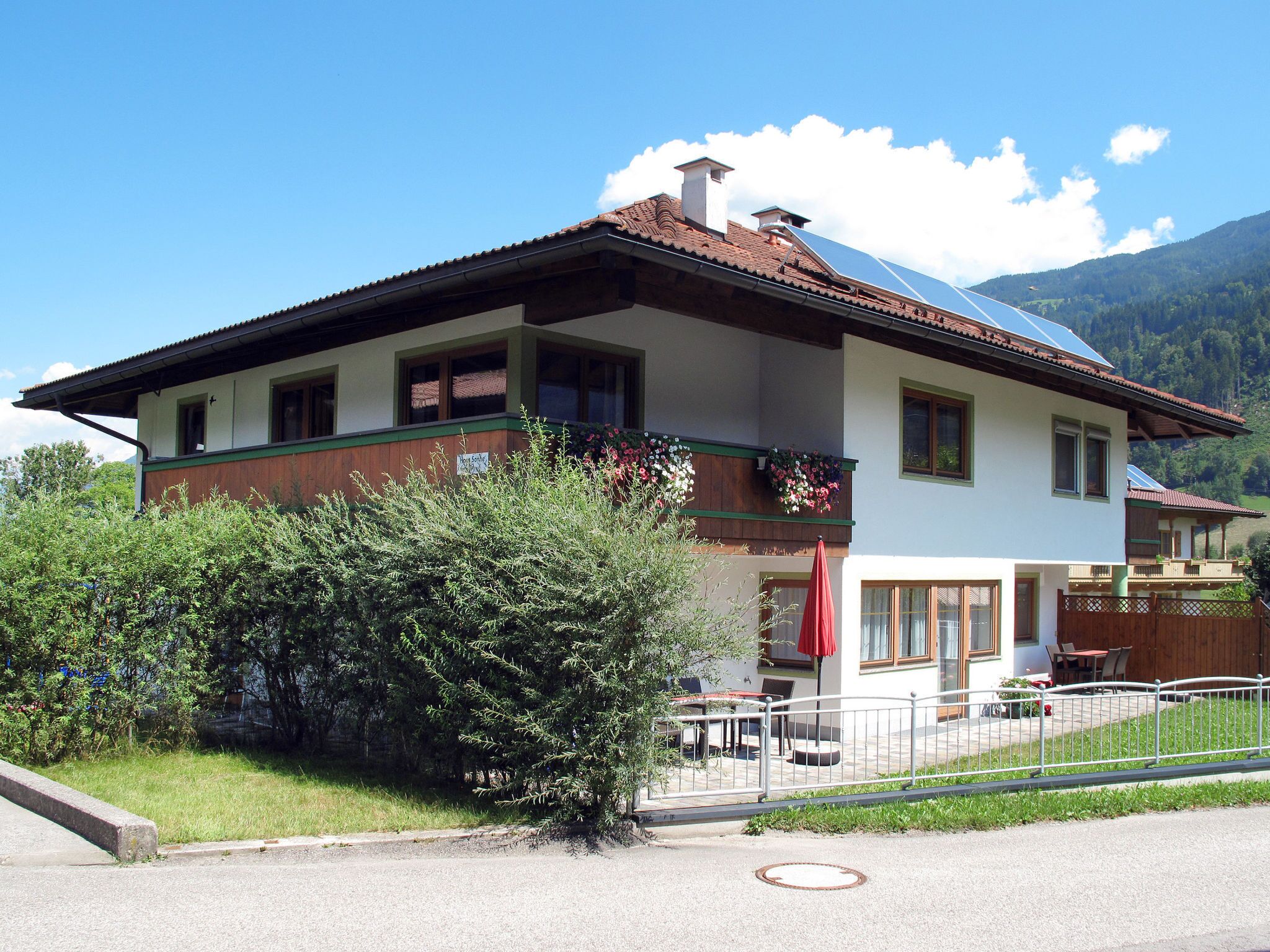 A two-story building with a sloped roof, a balcony with flowers, and a red umbrella.