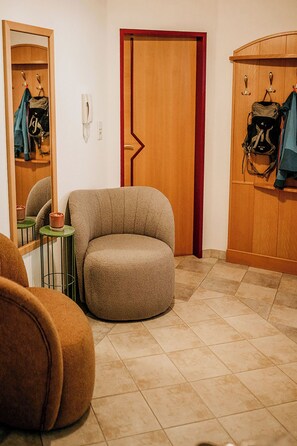 Une pièce avec un fauteuil rond de couleur beige, une porte en bois et un porte-manteau sur lequel est posé un sac à dos.