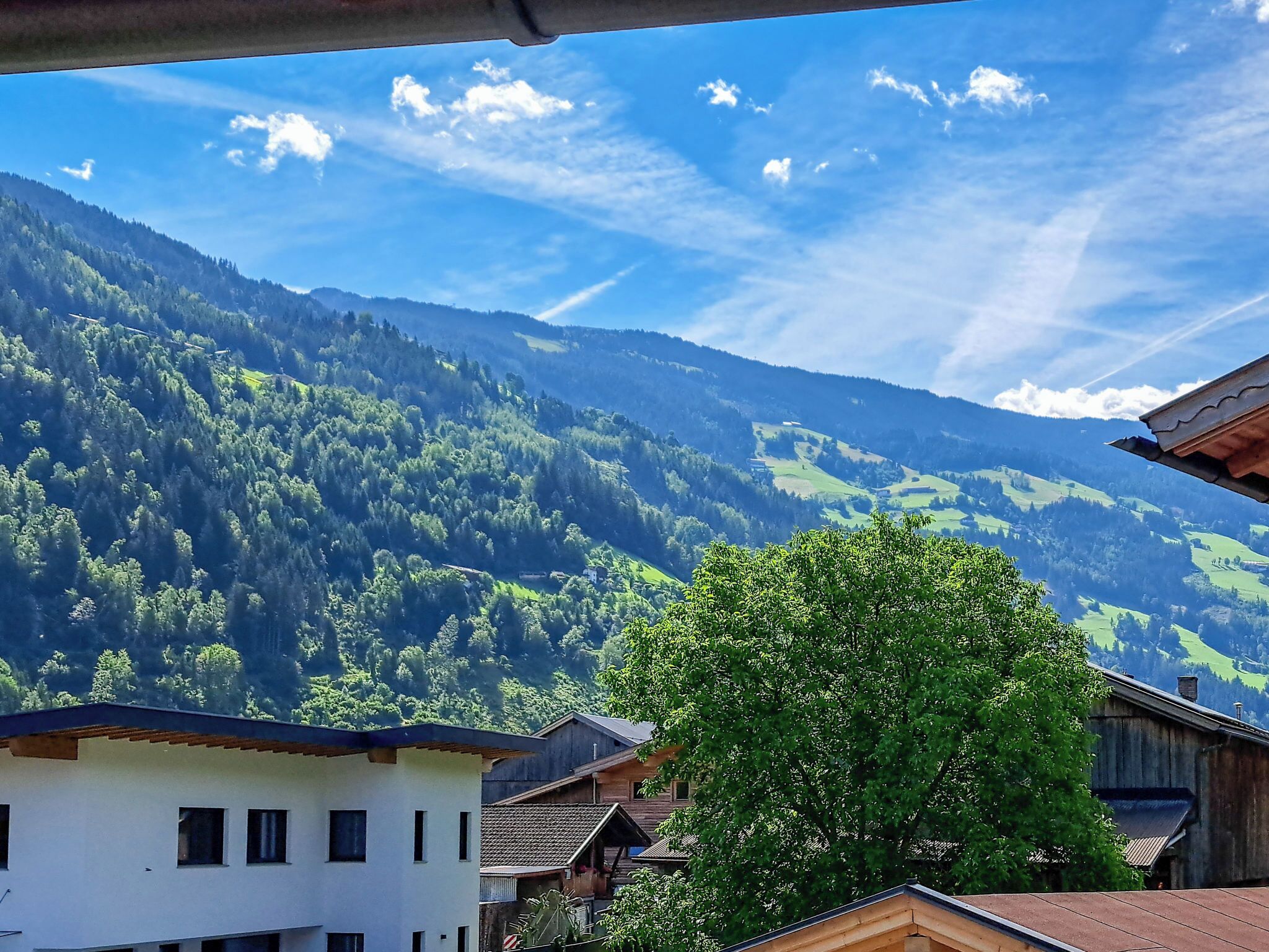 A mountain landscape with a clear sky, a tree in the foreground, and traditional buildings.