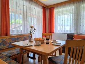 Un coin repas avec une table dressée pour deux personnes, un vase rempli de fleurs et un panier de pain.