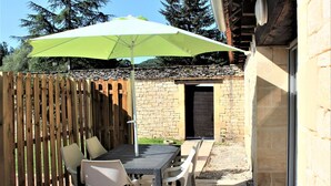 Une terrasse extérieure avec une table et des chaises, un parasol vert et une clôture en bois.