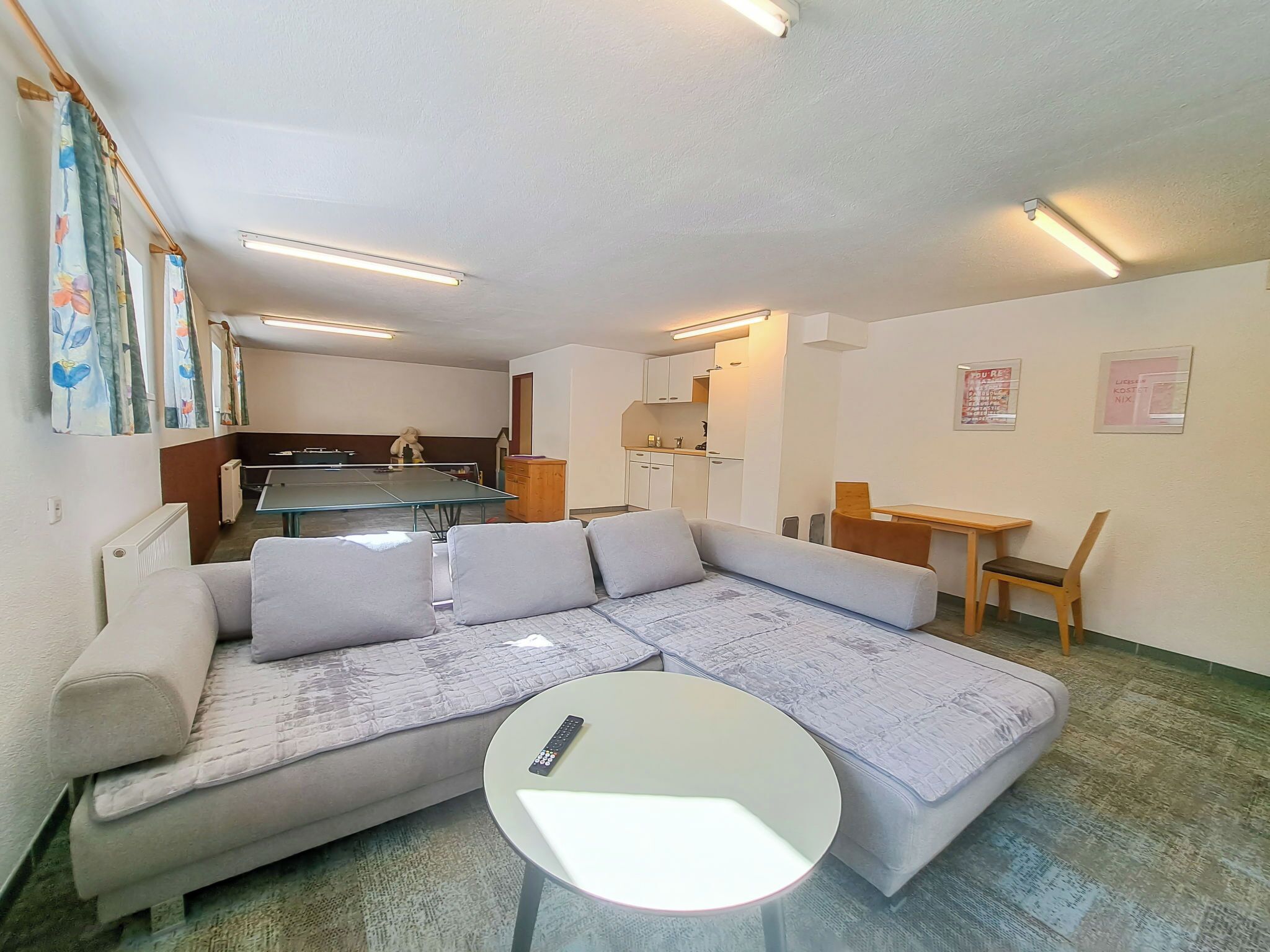 Una sala de estar moderna con un sofá modular, una mesa redonda de centro, una mesa de comedor y una zona de cocina al fondo.